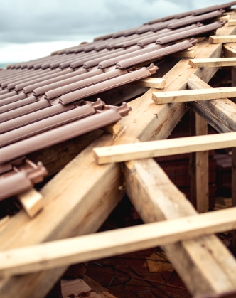Toiture en construction avec des tuiles marron posées sur une charpente en bois apparente sous un ciel couvert.
